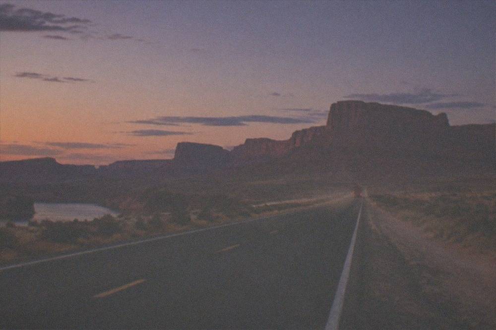 An empty desert highway running toward red rock formations at dusk