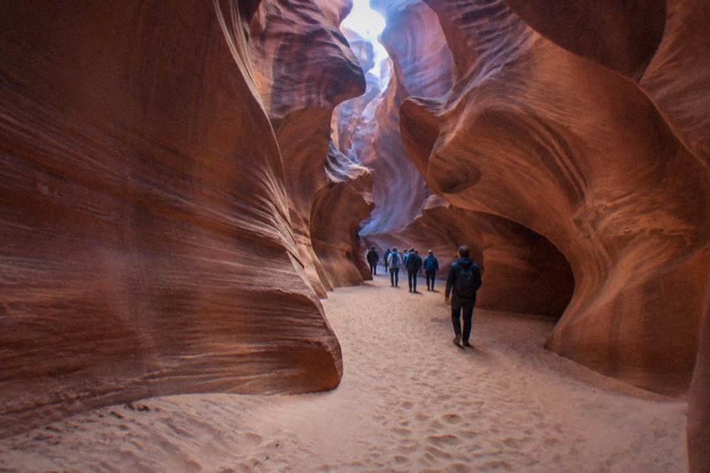 A guided walking group moving through a wide sandy passage between tall red canyon walls