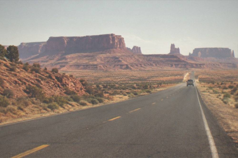An open desert highway stretching toward red rock mesas under a wide blue sky