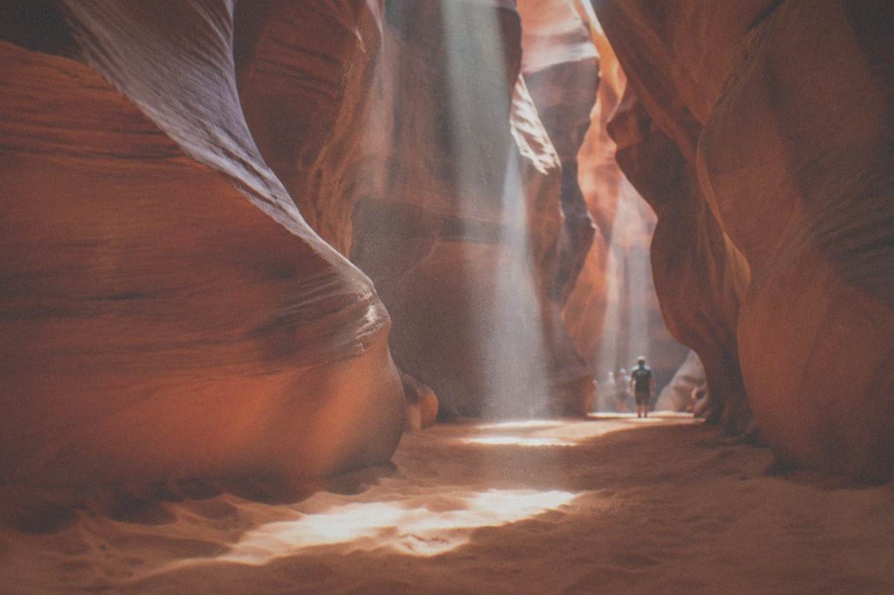 Sunlight beams falling into a narrow sandstone slot canyon with smooth curved walls