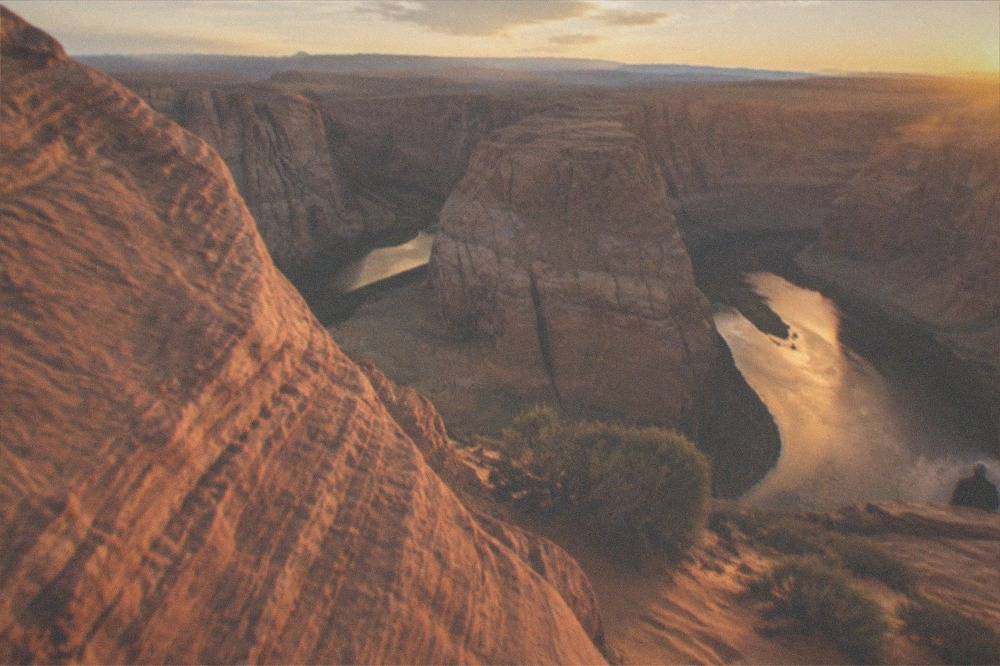 Wide view of a horseshoe-shaped river bend below red rock cliffs at golden hour