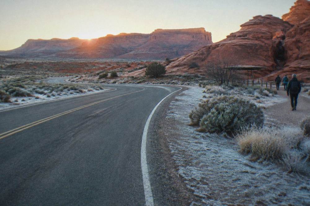 A desert highway stretching toward distant red rock mesas under a wide morning sky