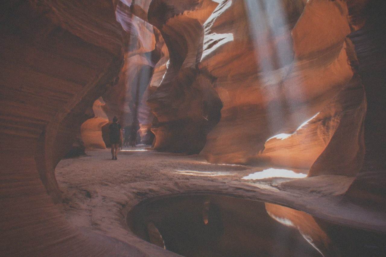 Sunbeams falling through a narrow sandstone slot canyon onto orange rock walls