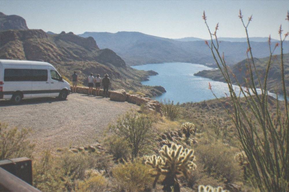 A tour van parked at a scenic overlook on the Apache Trail with Canyon Lake visible below.