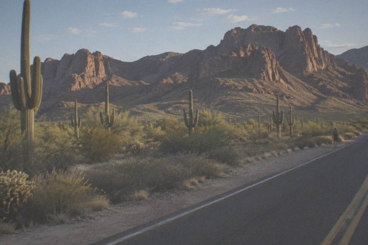 A panoramic view of the Superstition Mountains rising behind Apache Junction, with saguaro cacti dotting the desert landscape under a clear sky.