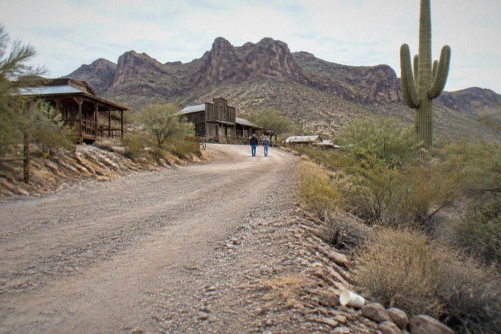 Desert hills above a western town in warm afternoon light with a gravel road leading toward the buildings