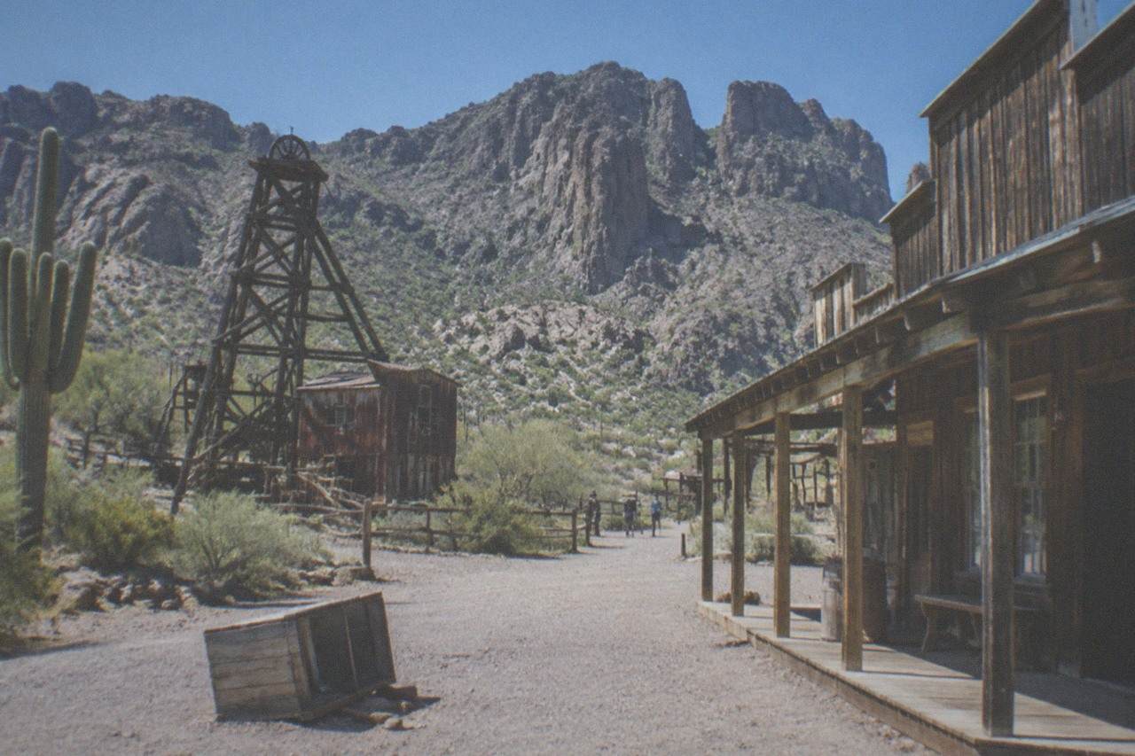Wooden false-front buildings of a rebuilt western mining town at the base of rocky desert hills under a clear sky