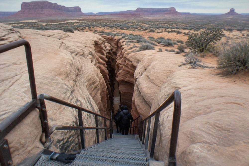 A metal staircase descending into a narrow slot canyon between smooth rock walls