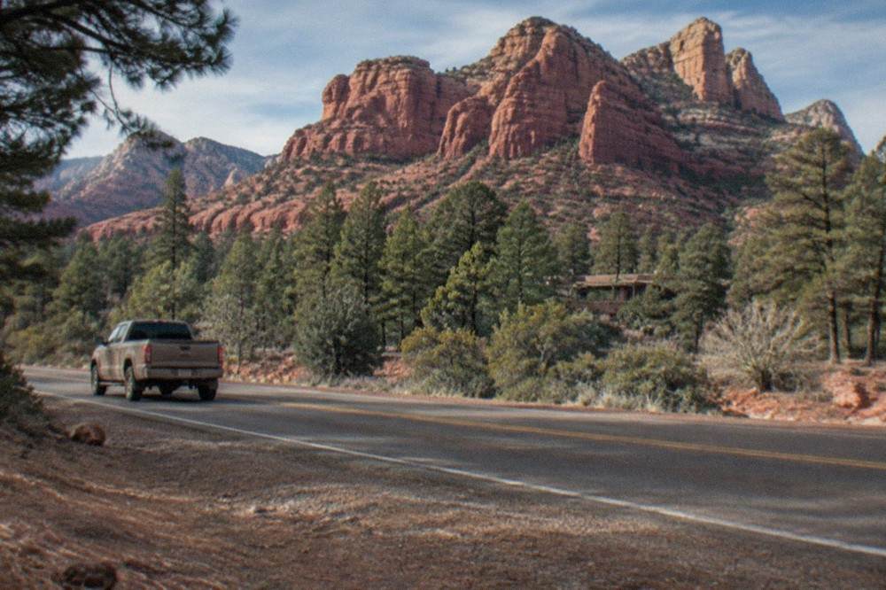 Red rock formations towering above pine trees along a scenic canyon road