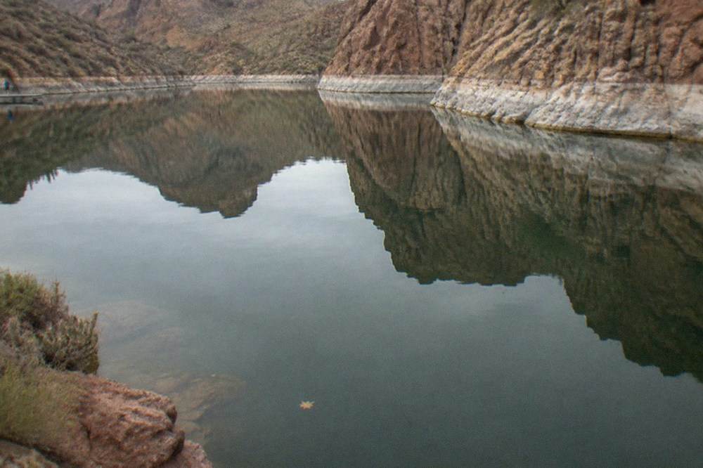 Rocky canyon walls reflected in the still water of a desert lake at midday