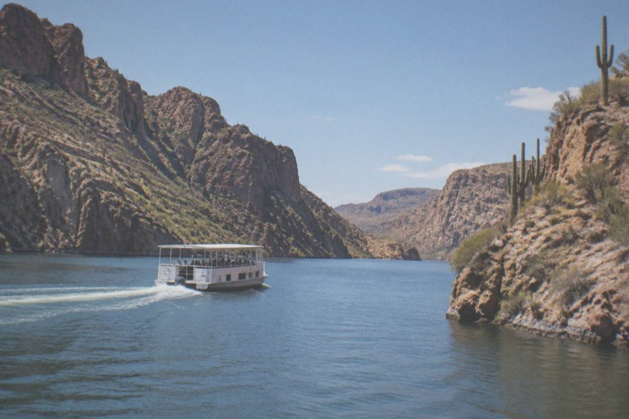 A sightseeing boat crossing a calm desert lake between steep rocky canyon walls