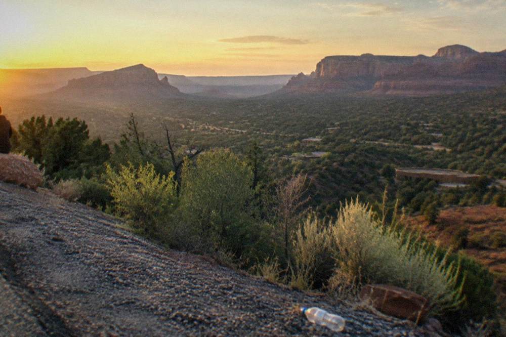 A highway shoulder viewpoint overlooking a wide valley with distant mesas at golden hour