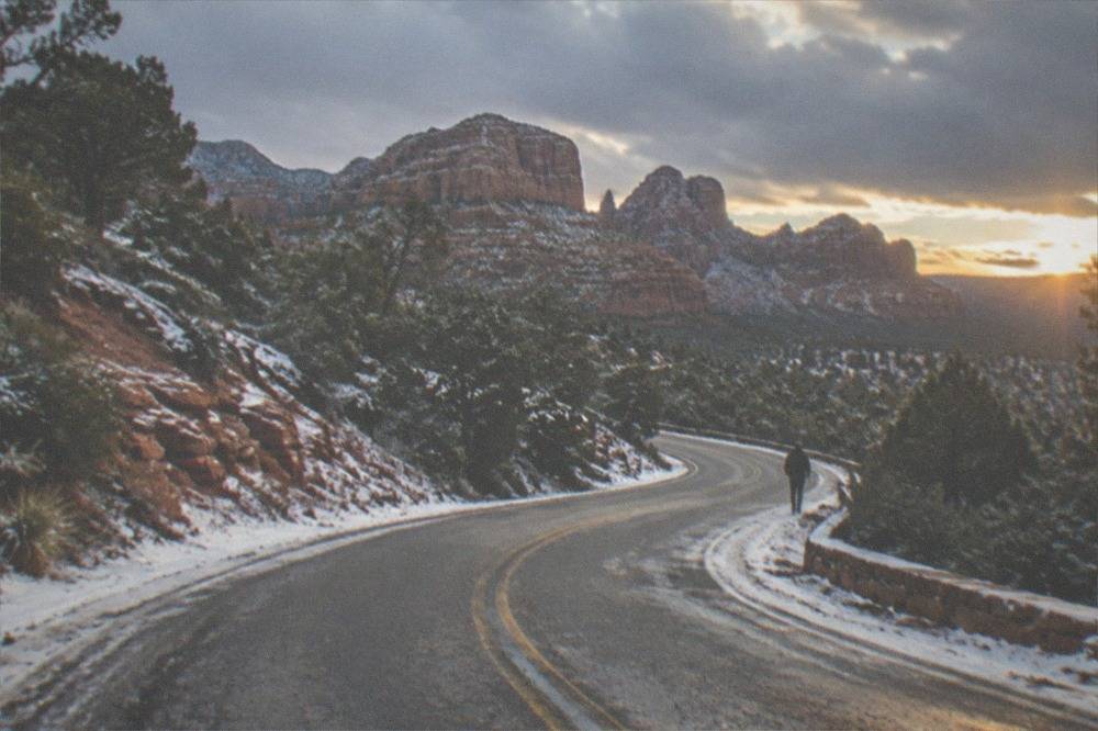 A winding road climbing through forested hills toward red rock cliffs in late afternoon light