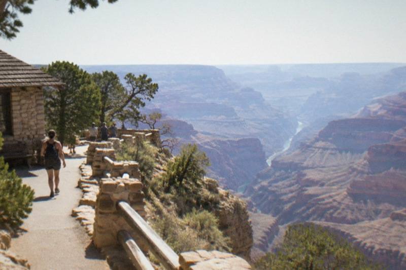 Layered red and gold walls of the Grand Canyon drop from the South Rim toward the river corridor under a wide desert sky.