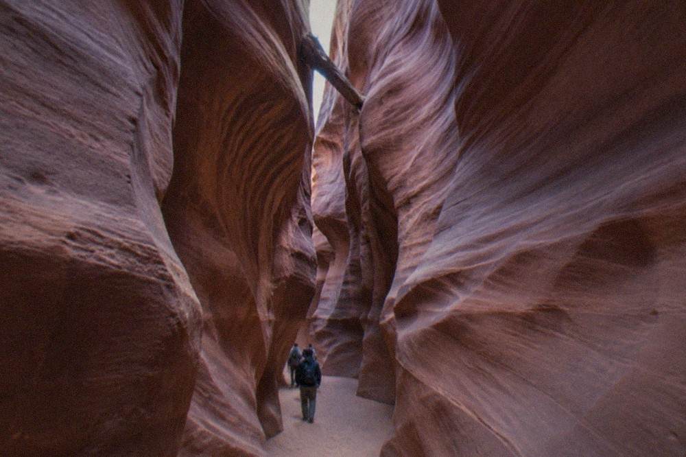 Curved orange sandstone walls of a slot canyon narrowing toward a sliver of sky