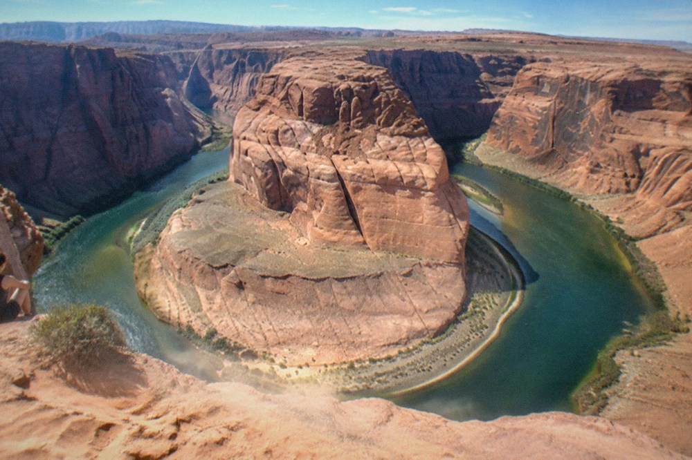 A sweeping river bend curving around a tall red rock cliff under a wide desert sky