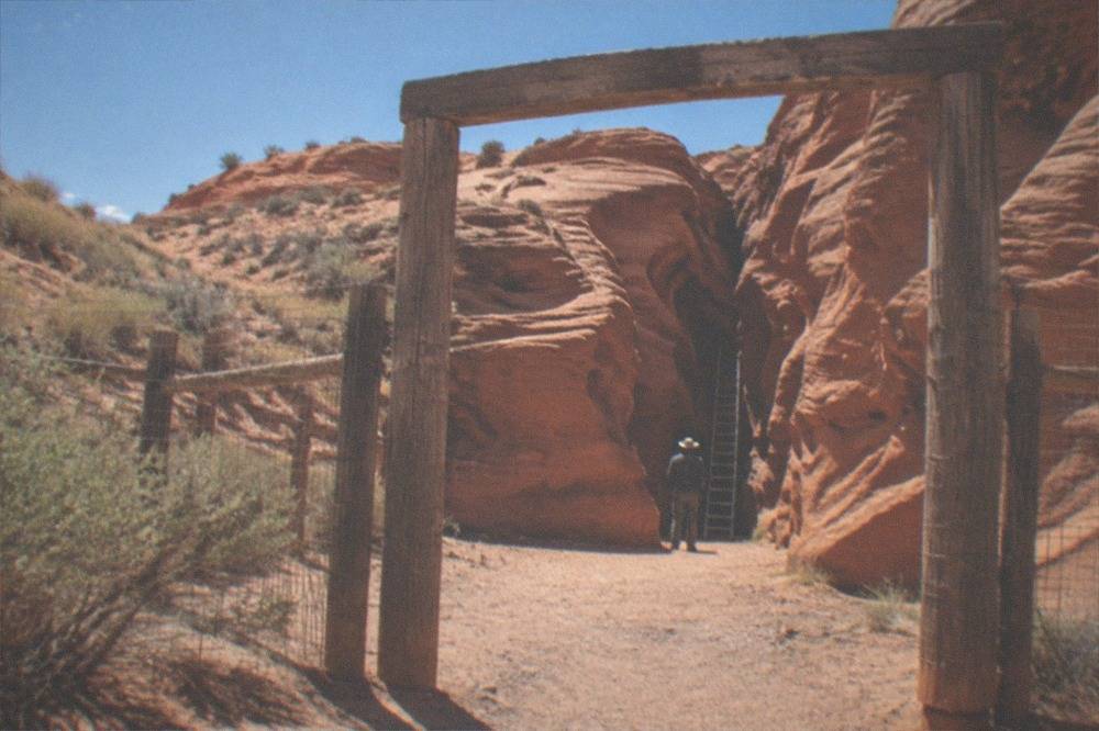 A canyon entrance area with a small wooden sign and red sandstone cliffs under a clear blue sky