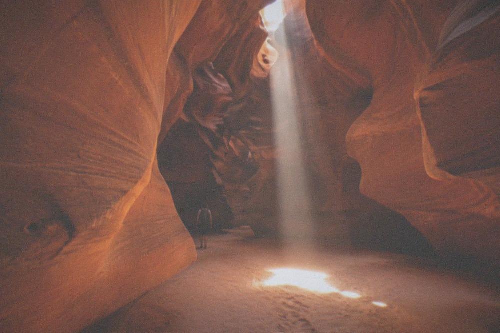 Sunlight beaming down through a narrow opening at the top of a slot canyon onto the sandy floor