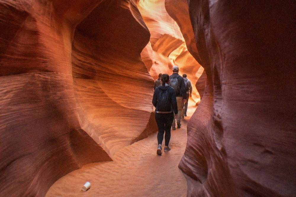 A guided walking group moving single file through a narrow curving slot canyon passage