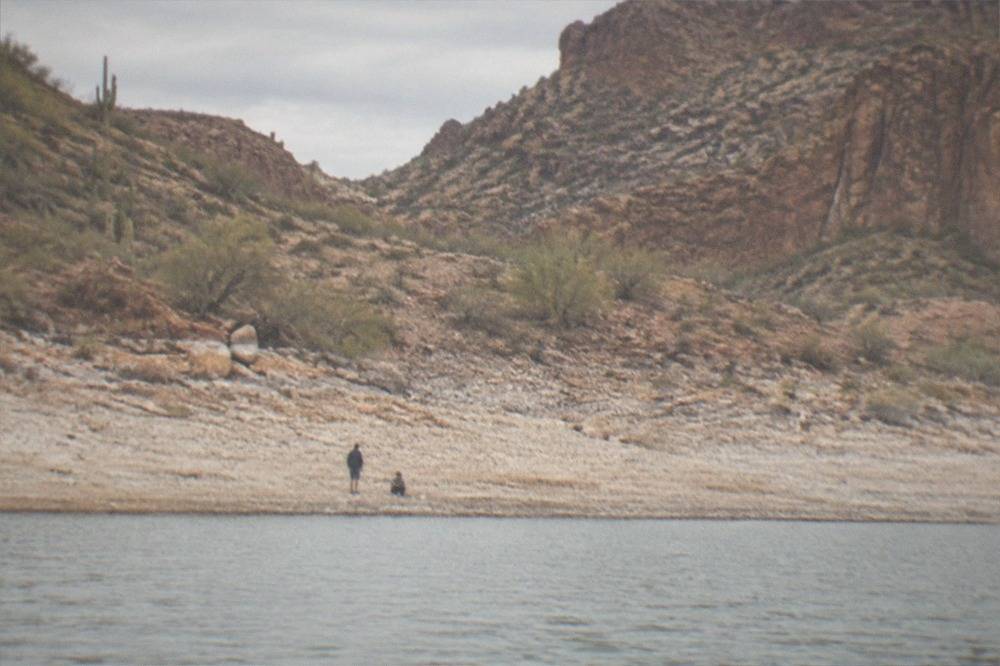 A lake shoreline with red rock walls and a wide band of exposed gravel below the high-water mark