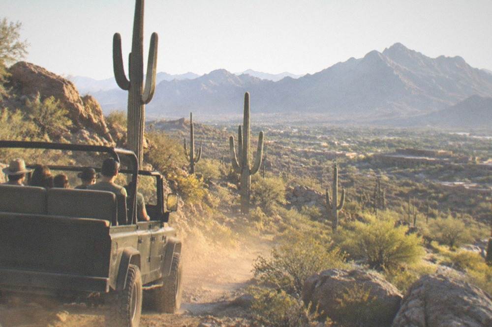 An open-top jeep on a rocky desert trail among tall saguaro cacti
