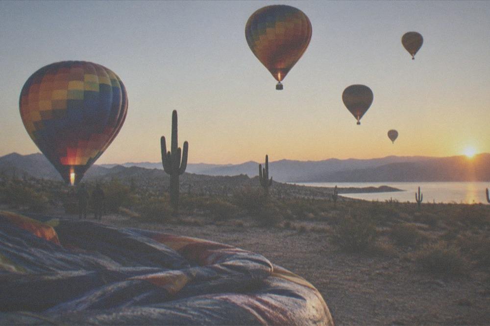 Hot air balloons floating over open desert at sunrise