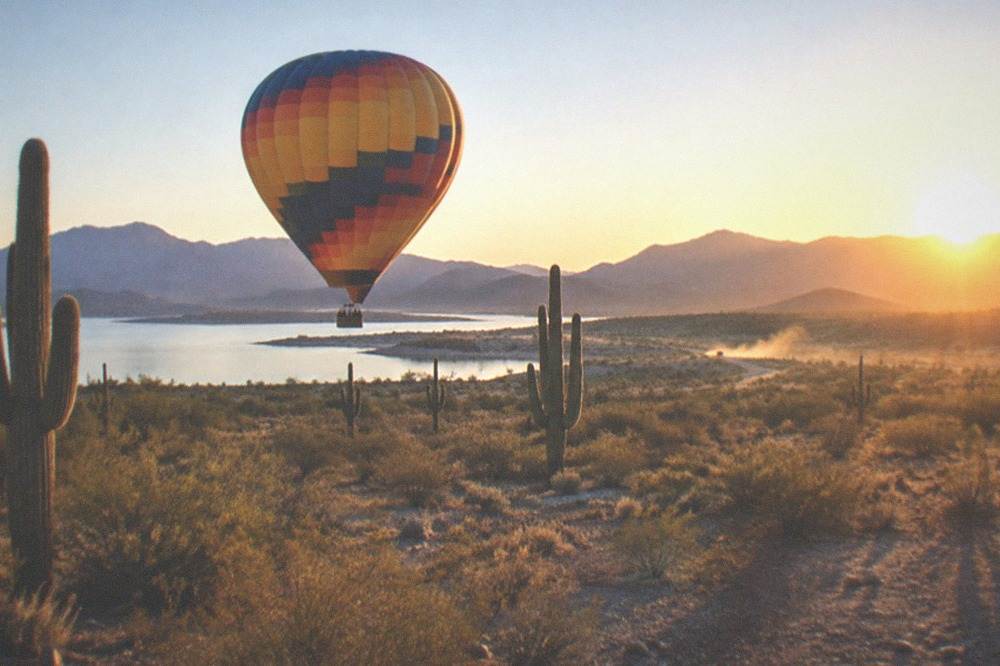 Hot air balloon floating low over the Sonoran Desert at sunrise with long shadows