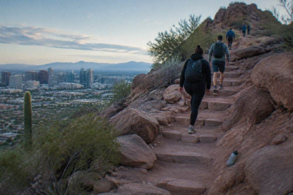 Steep red sandstone trail rising toward a rocky summit ridge in morning light