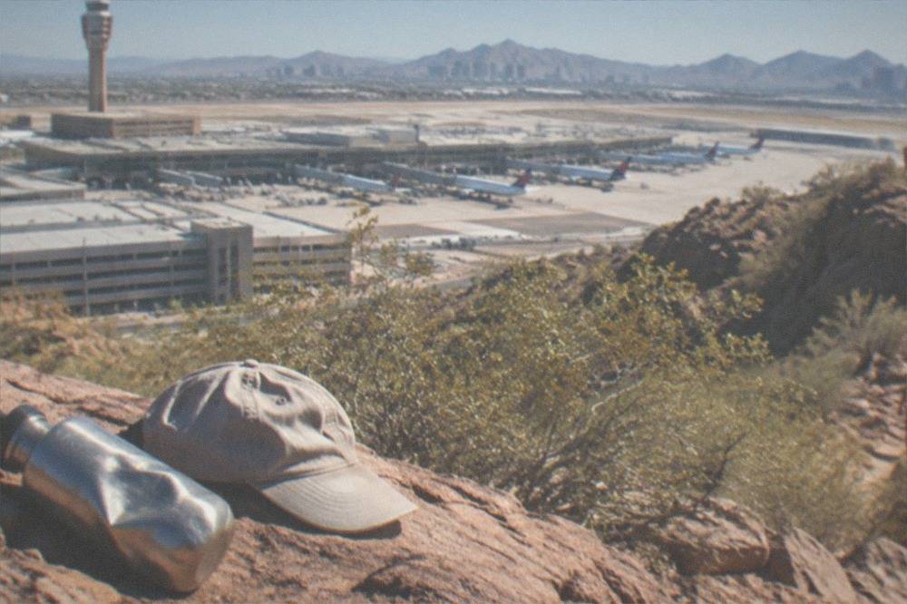A hiker's water bottle and hat resting on red rock beside a steep desert trail