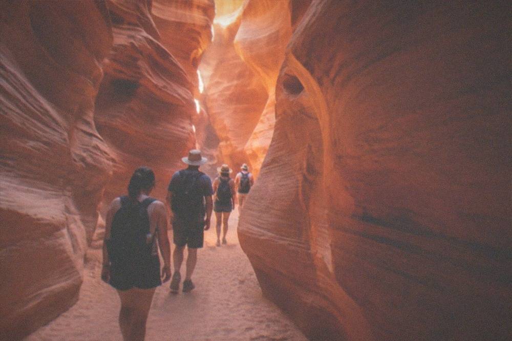 A guided group walking through a narrow sandstone slot canyon with light beams on the walls