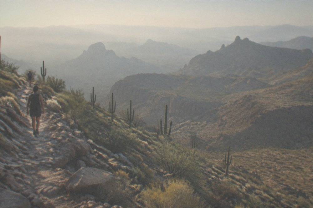 A rocky desert ridgeline trail with layered mountain ranges fading into haze