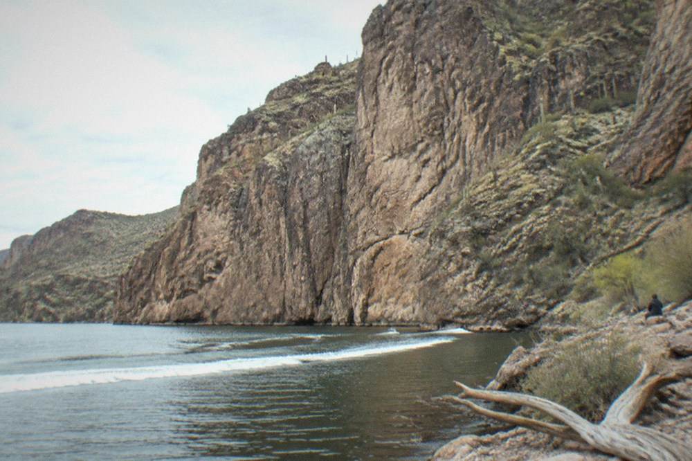 Rock walls of Canyon Lake reflected in still water seen from a boat deck