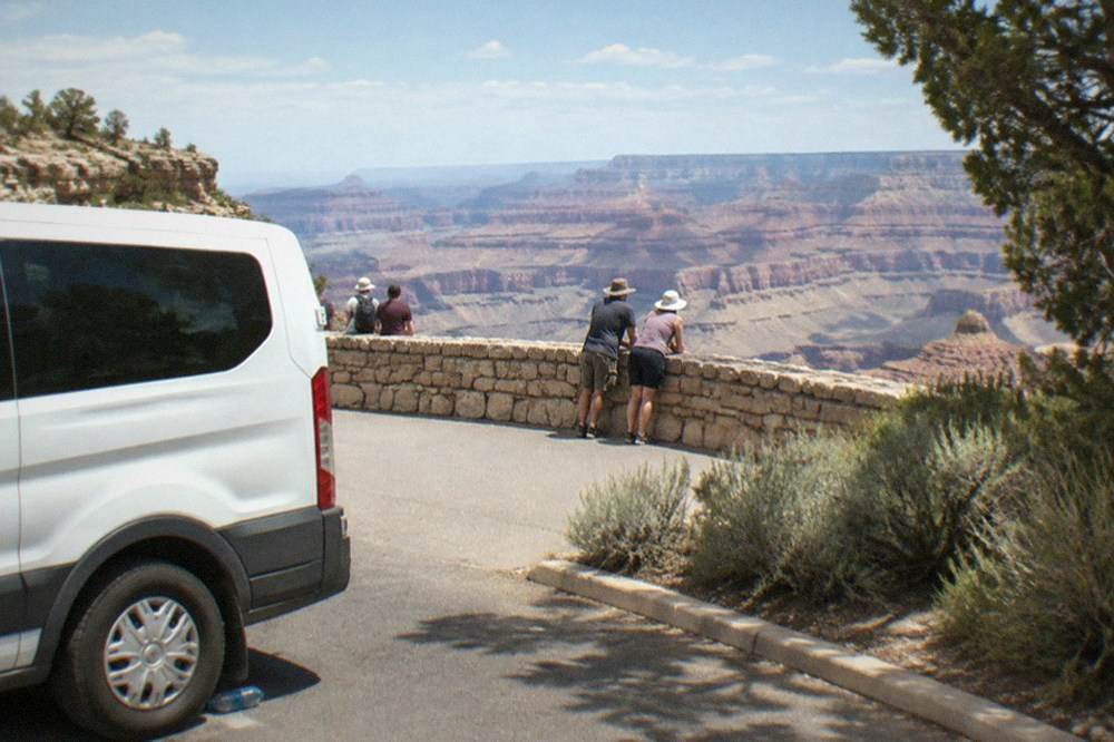 Tour van parked at a canyon overlook with visitors standing near the railing