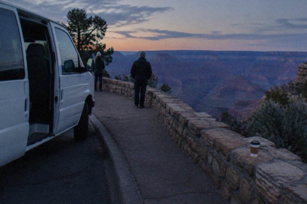 A tour van parked at a Grand Canyon South Rim overlook with layered canyon walls in the distance