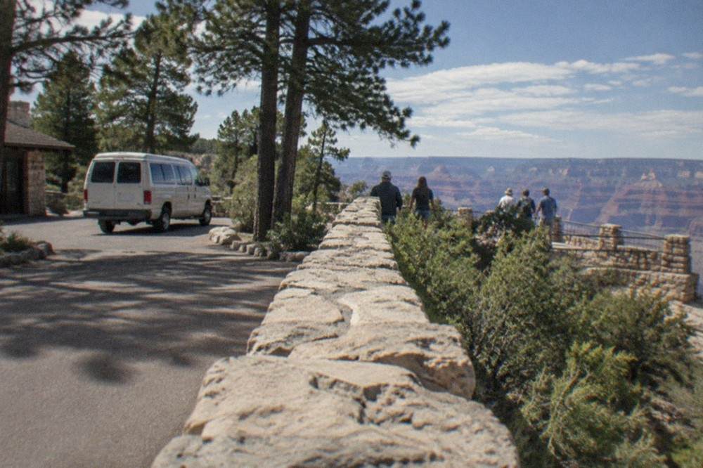 A tour van parked at a Grand Canyon overlook with pine trees