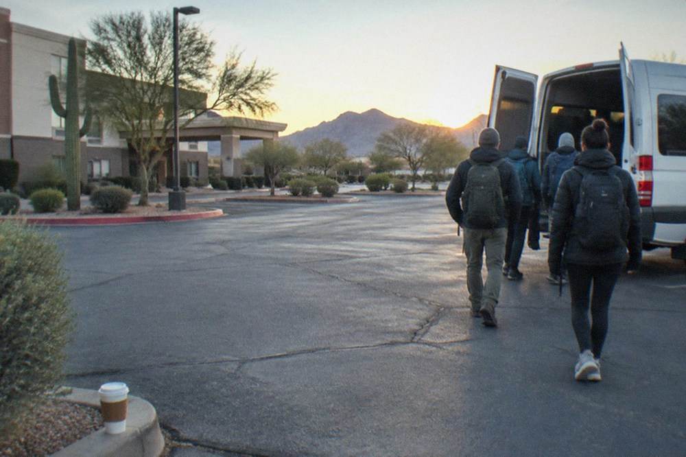 Passengers boarding a tour van in a hotel parking lot at sunrise