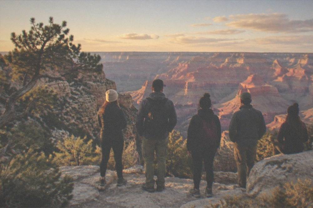 A small group standing at a rocky Grand Canyon viewpoint in late afternoon light