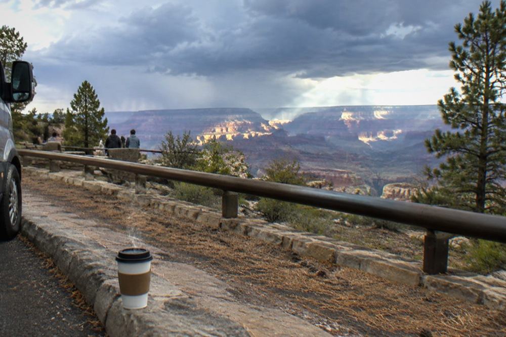A passenger van parked at a scenic overlook with canyon walls rising beyond the guardrail