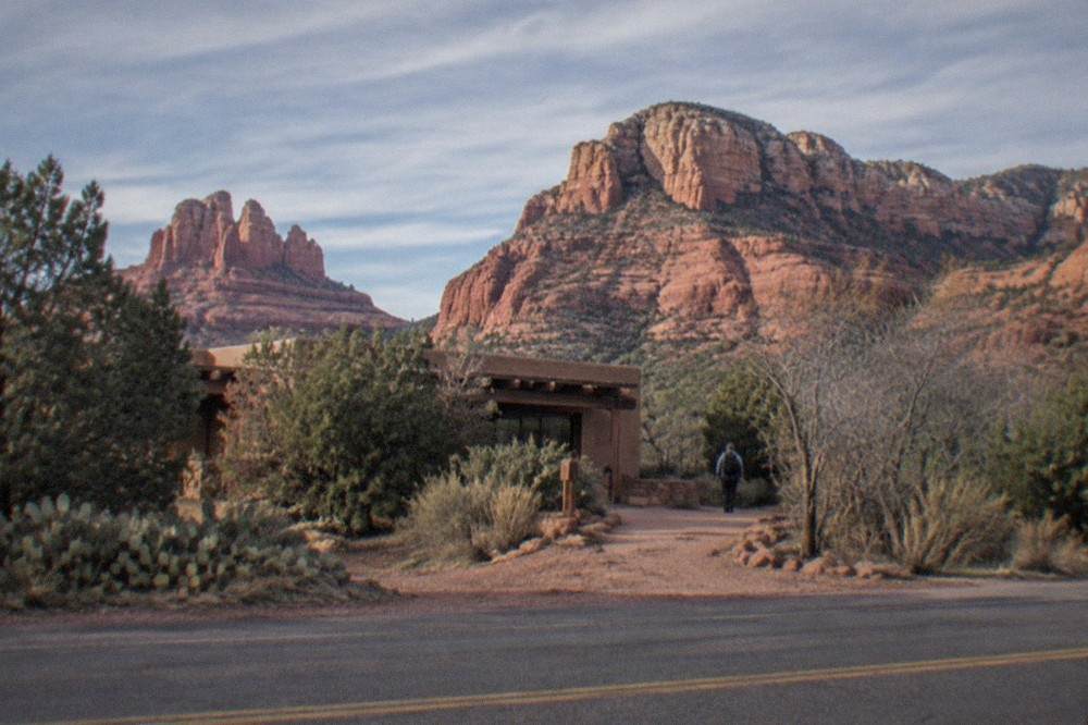 Red rock formations rising above a road lined with juniper trees