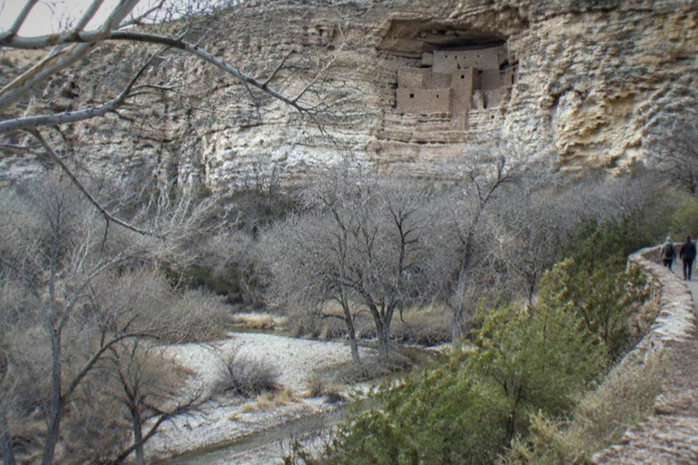 A stone cliff dwelling built into a recess in a tan rock cliff face