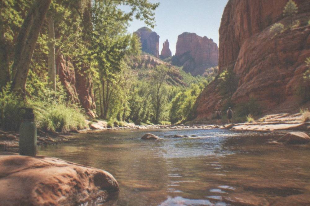 A creek running between tall red rock canyon walls with trees along the banks