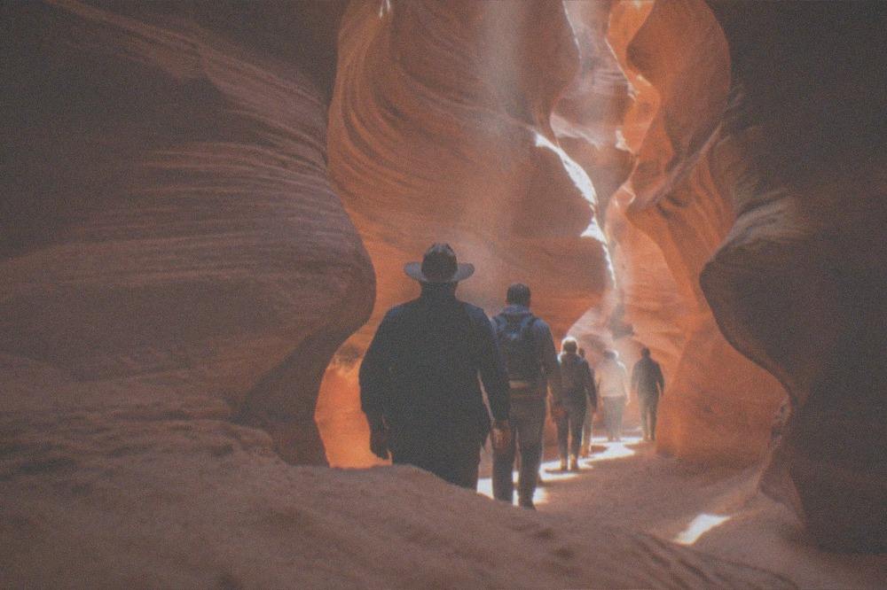 A guided group walking single file through a wide slot canyon corridor