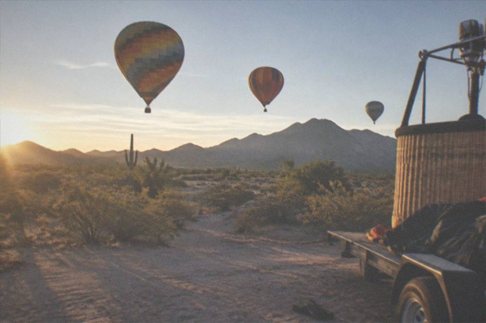 Several hot air balloons floating low over open desert at sunrise with long shadows across the ground