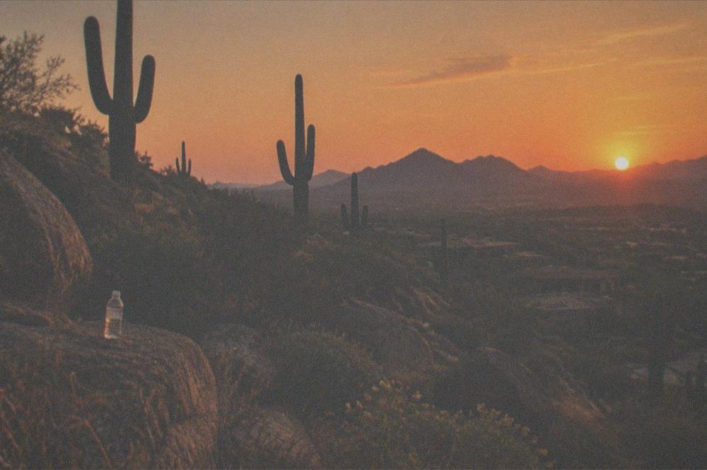 Golden sunset light over desert hills and saguaro cactuses with a deep orange sky