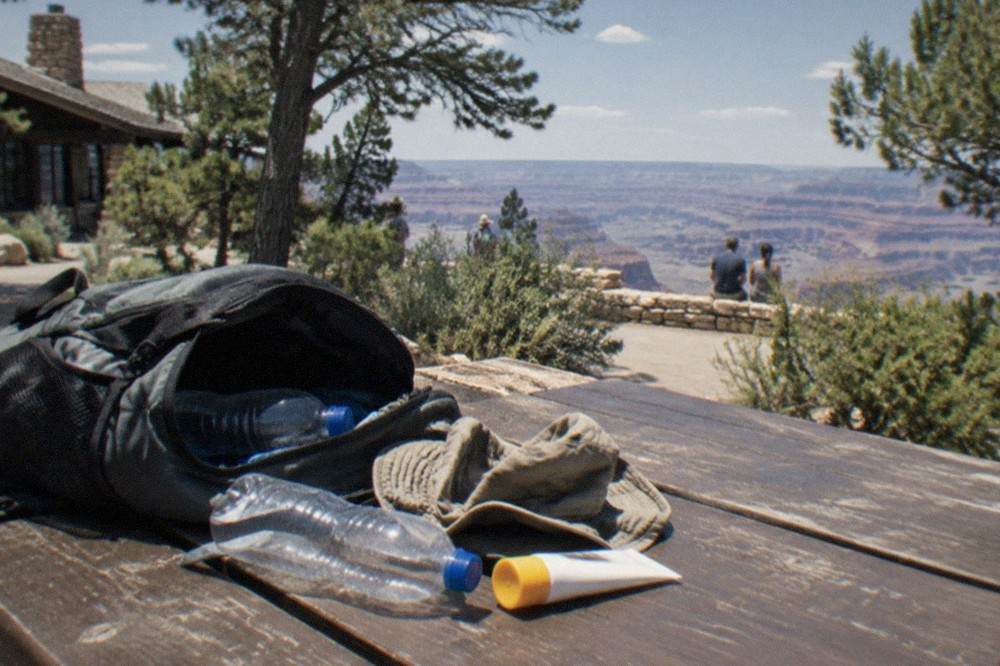 Open daypack with water bottles, hat and sunscreen on a wooden bench