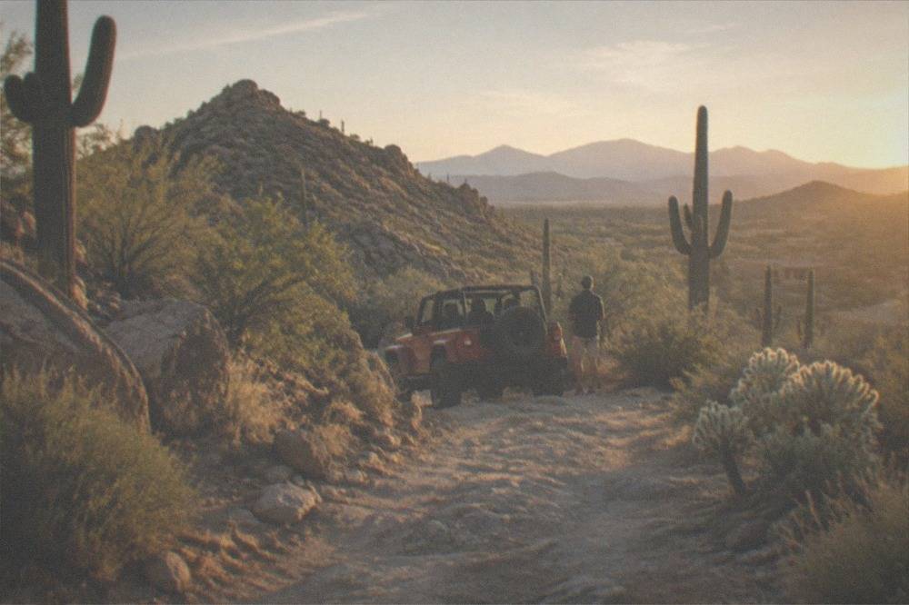 Red jeep parked on a desert trail with saguaro cacti and rock formations