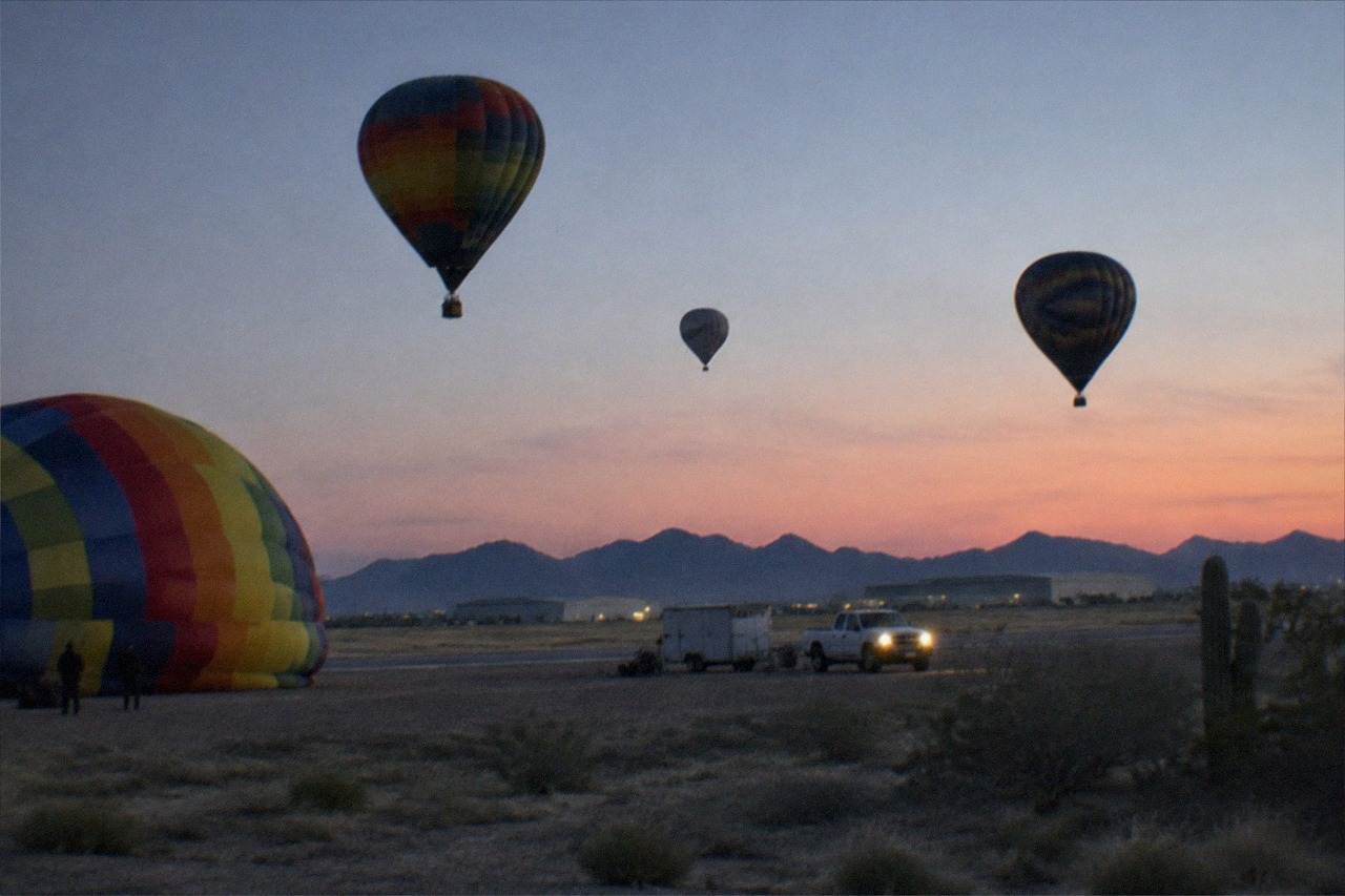 A cluster of hot air balloons drifting low over cactus-studded Sonoran Desert ground as the sun climbs.