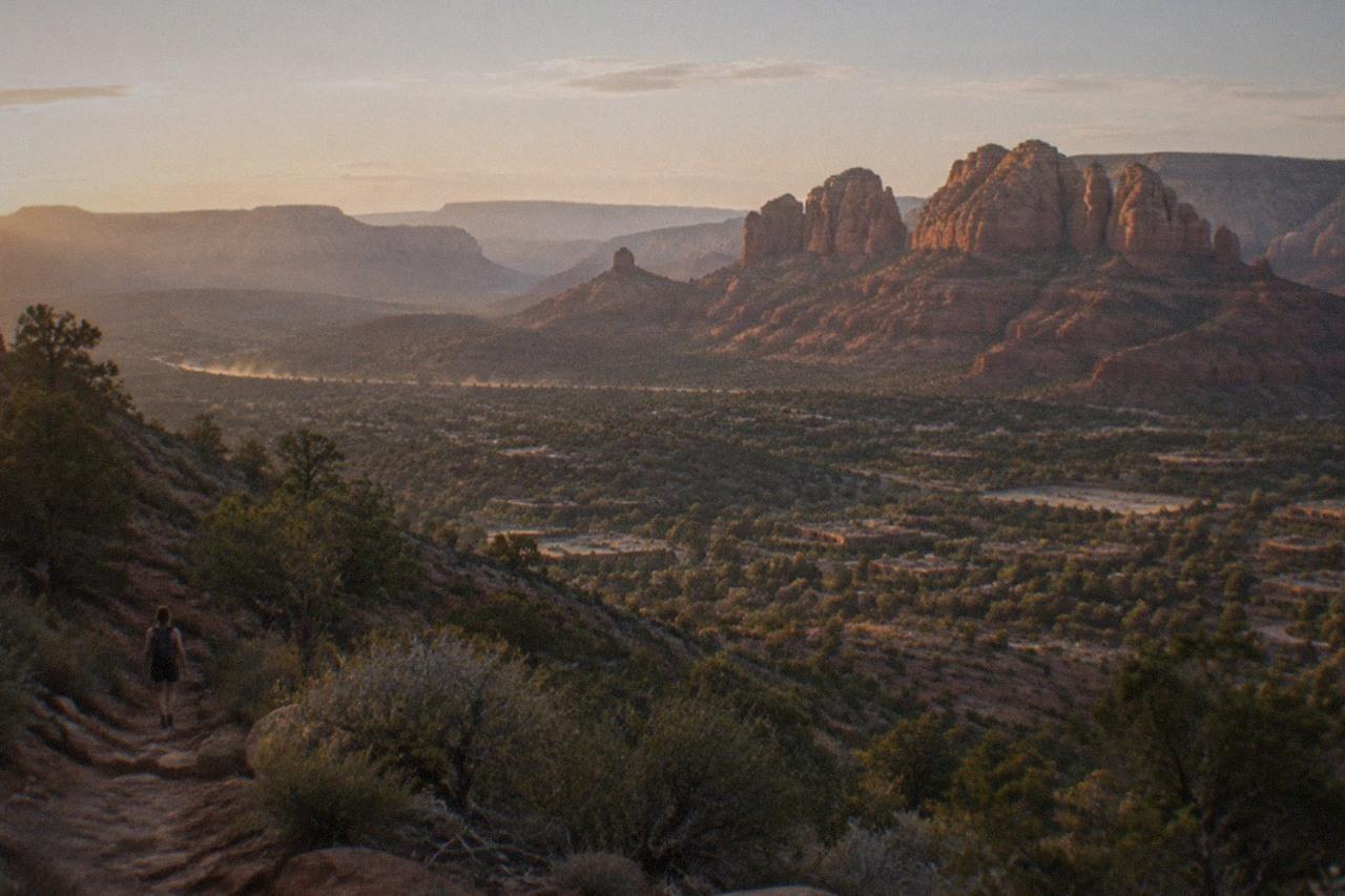 Red rock buttes of Sedona rising above oak-dotted hillsides, warm light on the sandstone in a wide desert view.